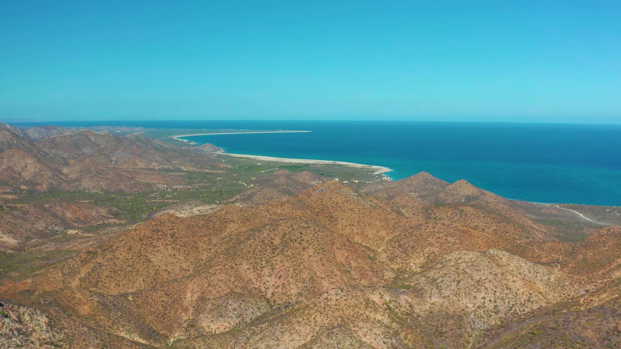 Second frame shows Cabo Pulmo's dry mountain ridges lower in frame, the coastline running across the middle distance, blue ocean at the horizon, and no visible people.