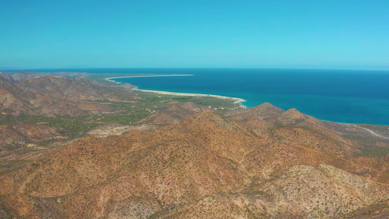 Aerial view in Cabo Pulmo, Baja California Sur showing sunlit brown hills, a green valley strip, the curving shore, and no visible people.