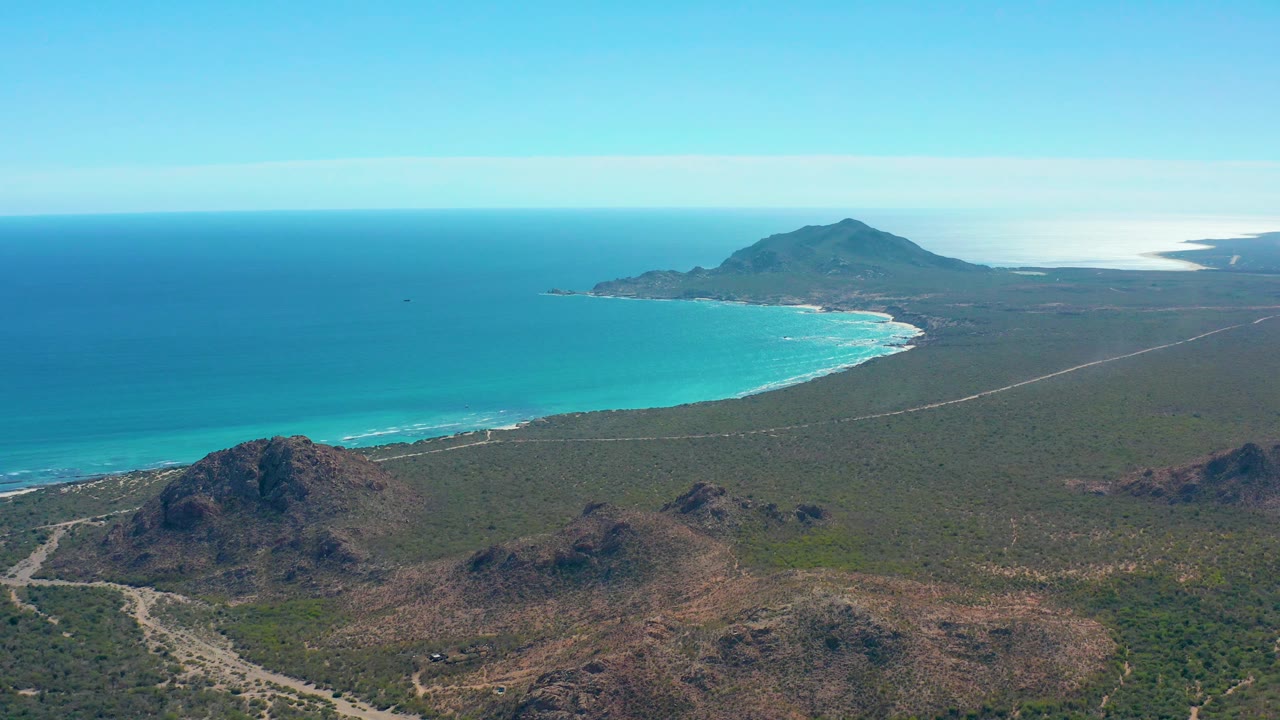 Coastal desert plain with rocky foreground hills, road, beach, and blue ocean.
