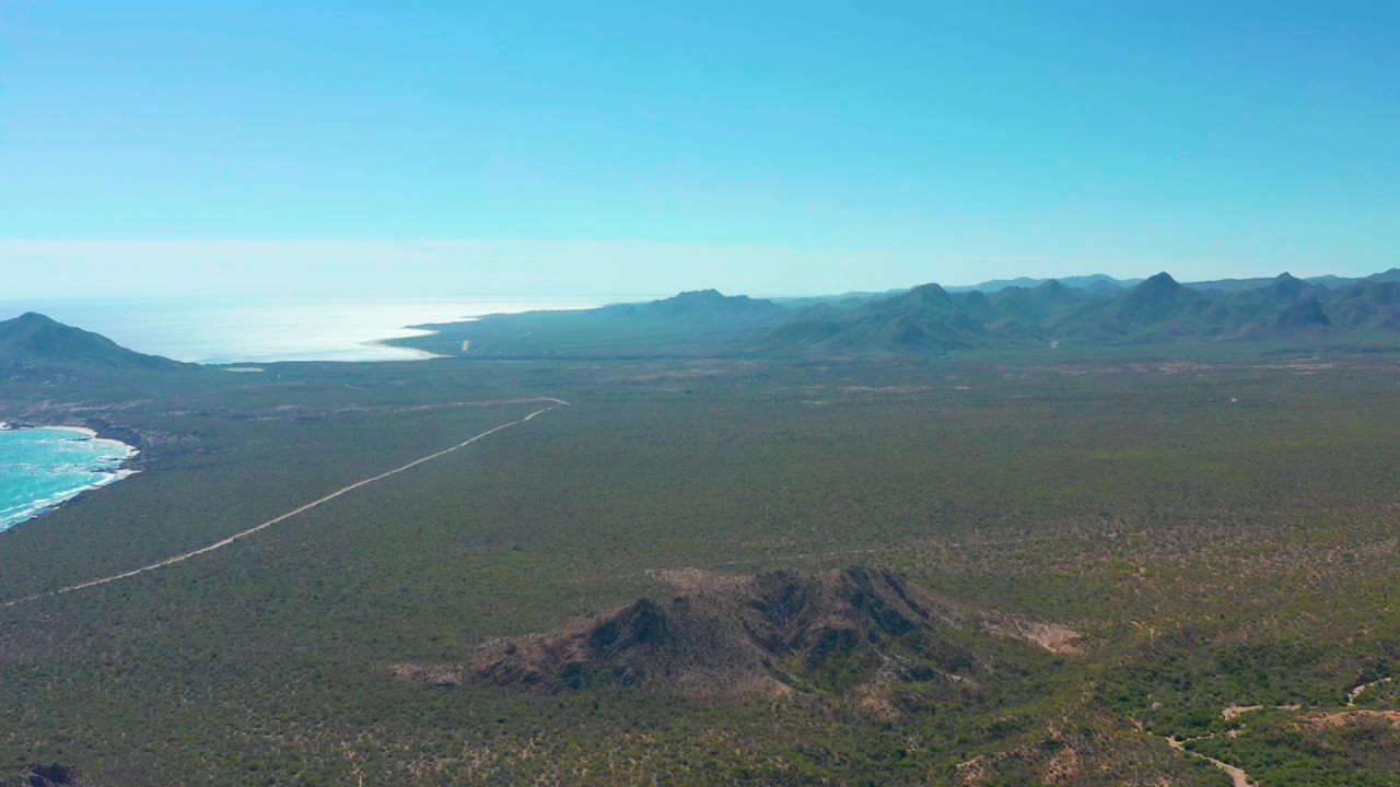 Aerial view of ocean, coastal plain, road, and distant mountains.