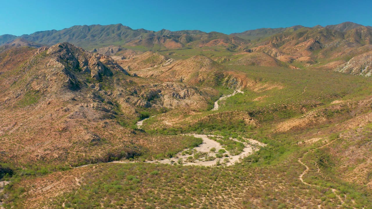 Aerial landscape with rocky foreground hills, valley vegetation, and distant mountains.