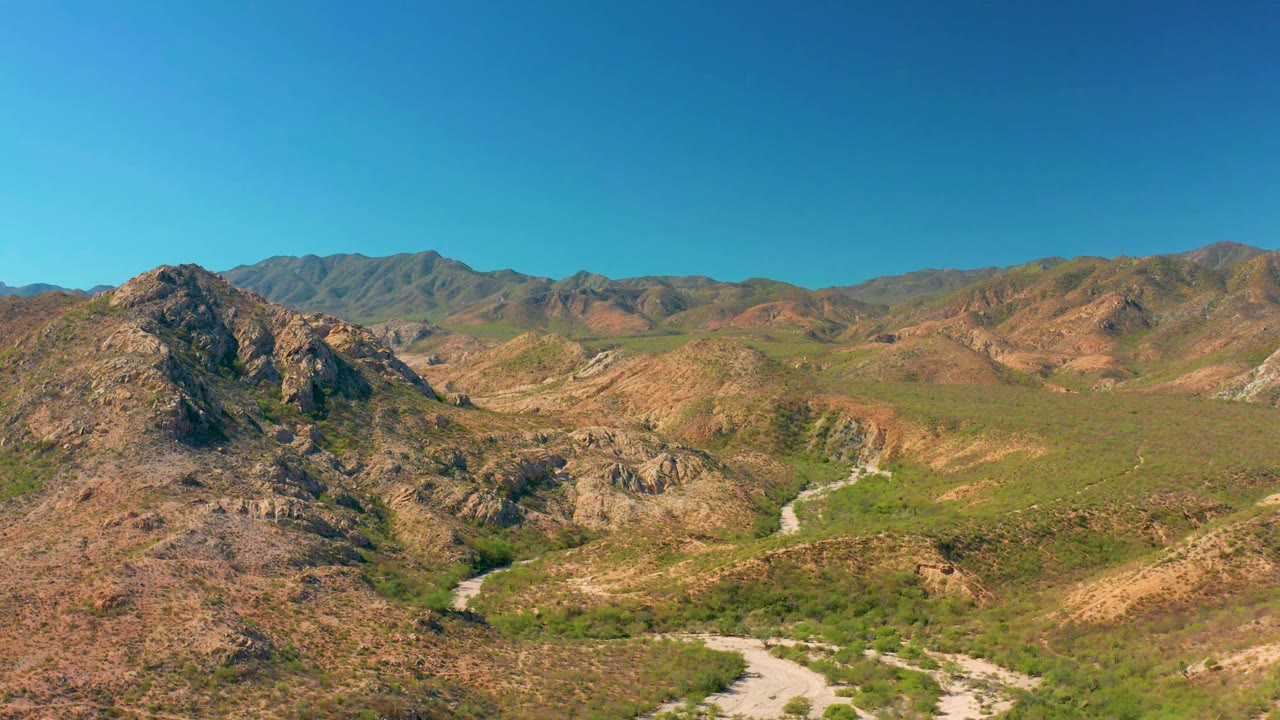 Cabo Pulmo aerial view with the central rocky outcrop more prominent, green vegetation across the valley floor, a pale river channel, and no visible people.