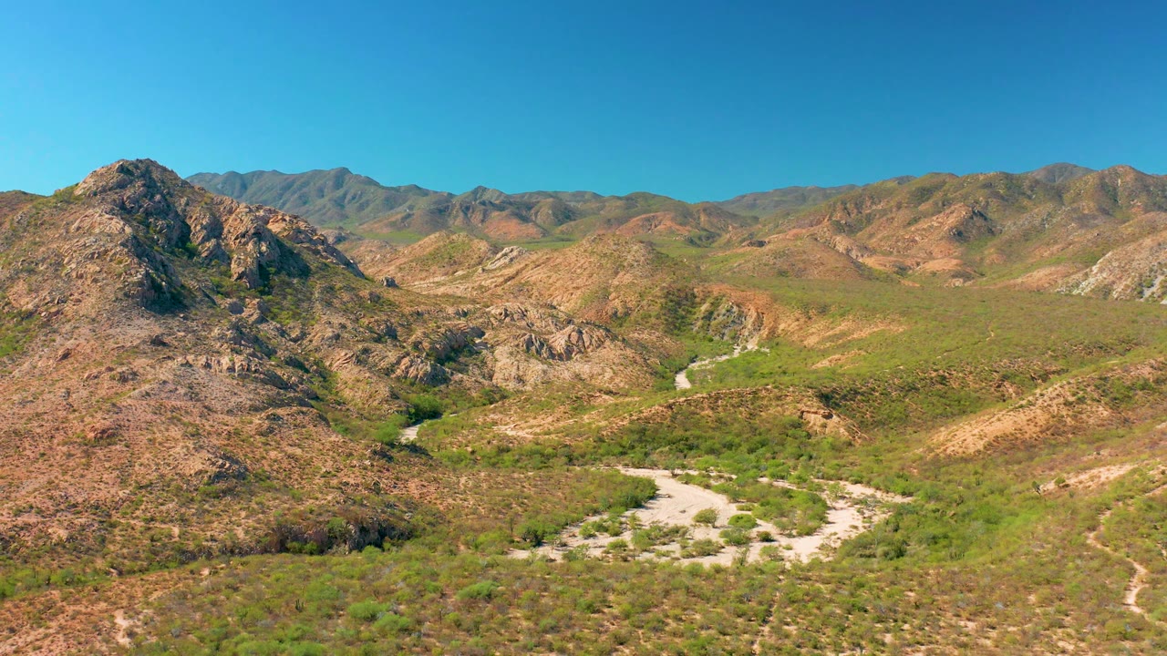 Elevated landscape view of dry hills, green valley growth, and winding road.