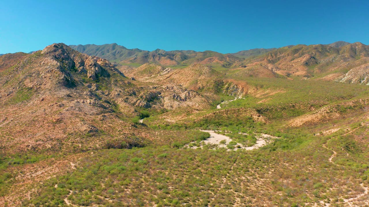 Cabo Pulmo mountain landscape seen from above, with the dry wash and winding road running through the midground, brown hills around it, and no visible people.