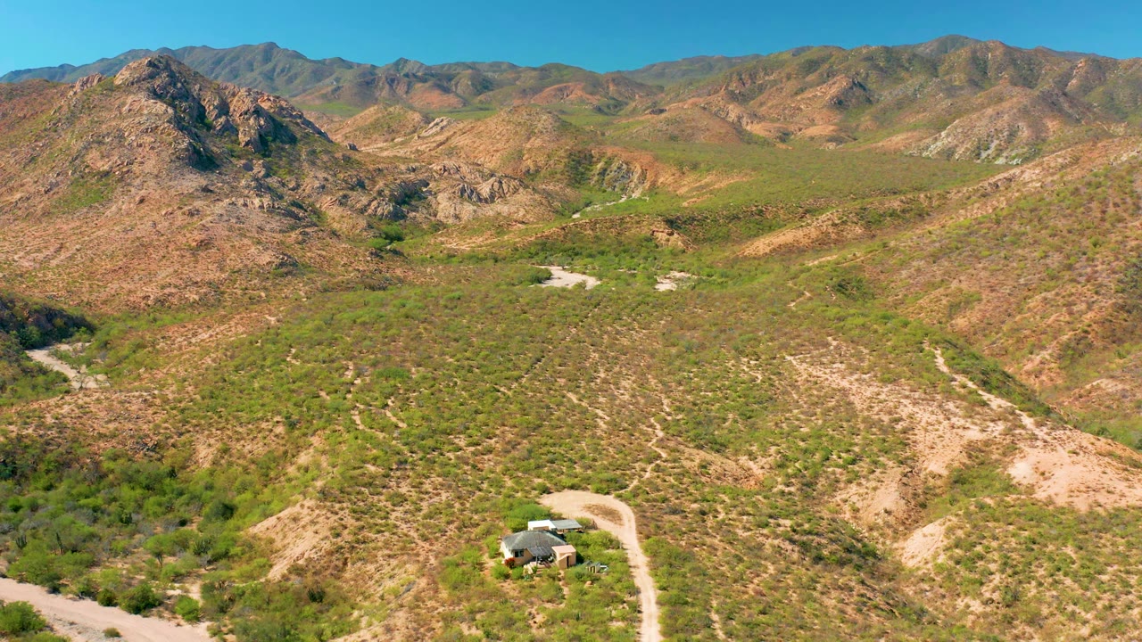 Aerial view in Cabo Pulmo with the road bending through scrub-covered hills, a small vehicle or roadside object near the lower foreground, and no visible people.