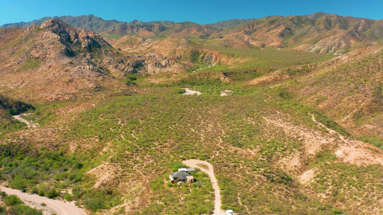 Cabo Pulmo aerial frame with a small vehicle on the light dirt road, dry washes and green brush spreading across the hills, and no visible people.
