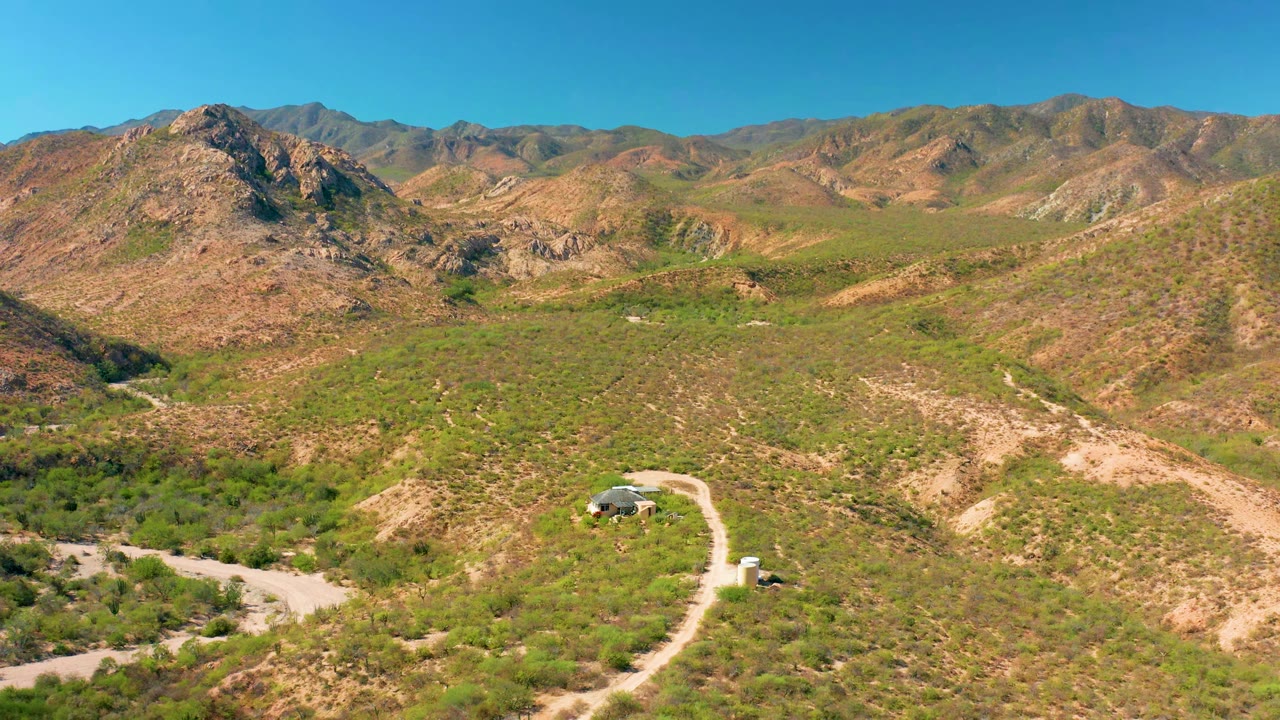 At 0:01, the small vehicle is visible on the curving road below scrub-covered hills and a broad mountain ridge in Cabo Pulmo, with no visible people.