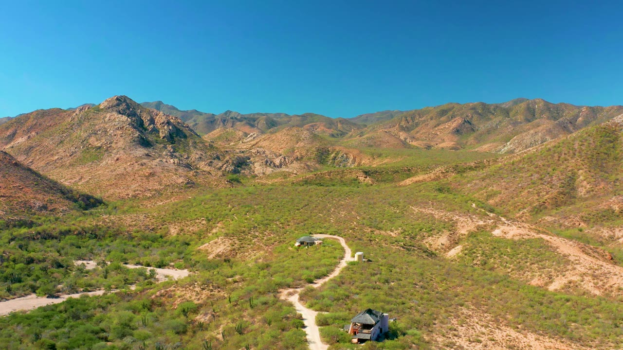 High aerial view of a winding dirt path through scrub and rocky mountains.