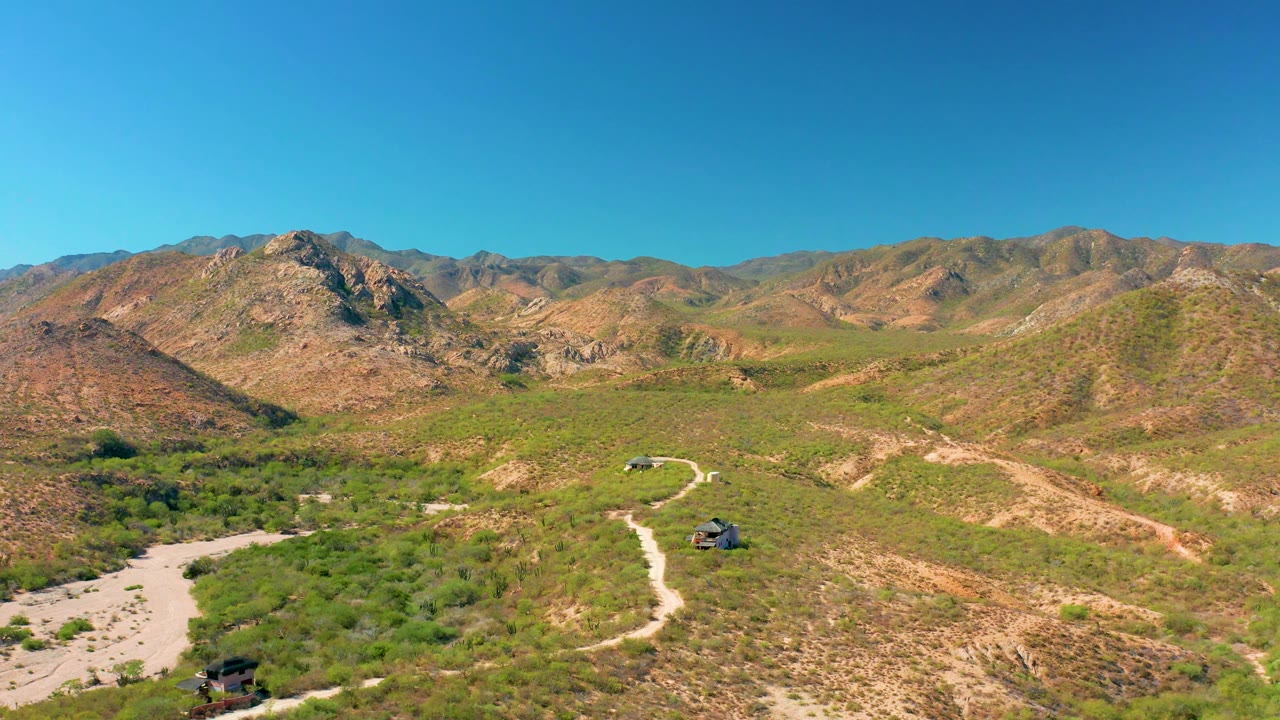 Aerial landscape with SUVs on a winding road below rocky mountains.