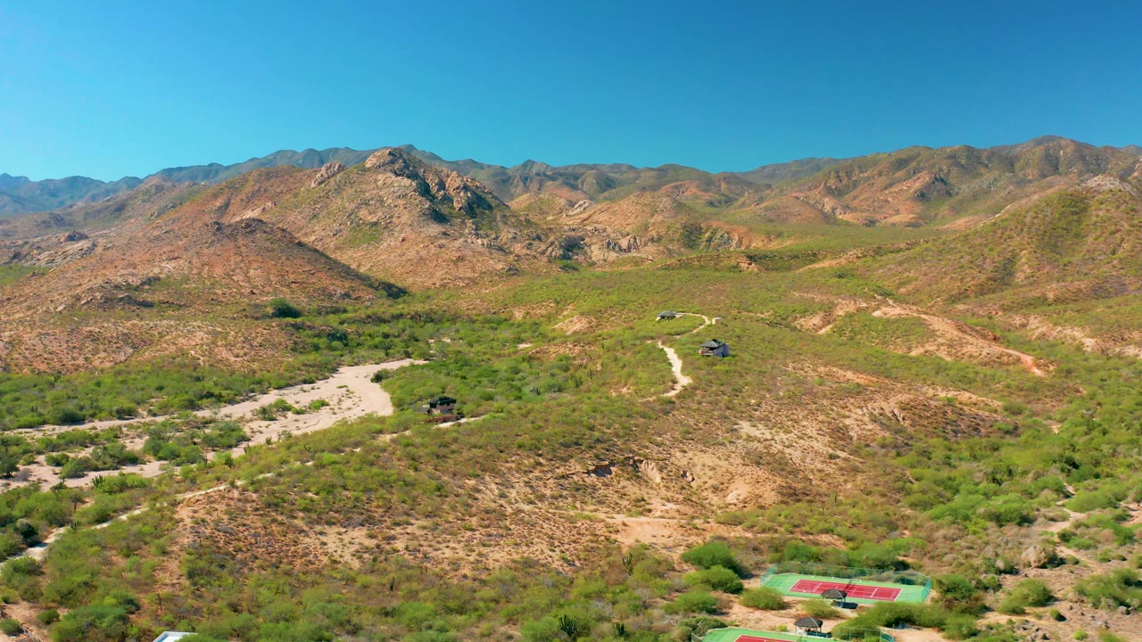 Cabo Pulmo aerial view with the pale road bending across the valley floor, scrubby vegetation in the foreground, rocky hills beyond, and no visible people.