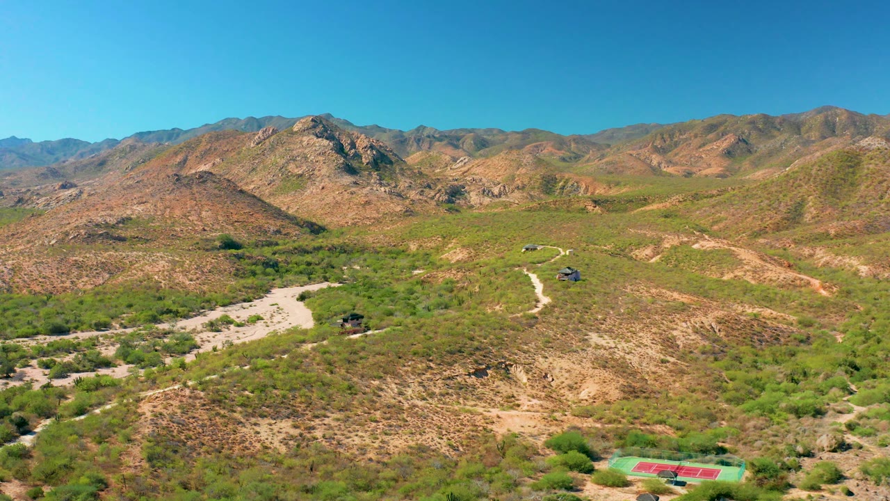 Aerial landscape with a rocky hill, desert vegetation, and a winding dirt road.