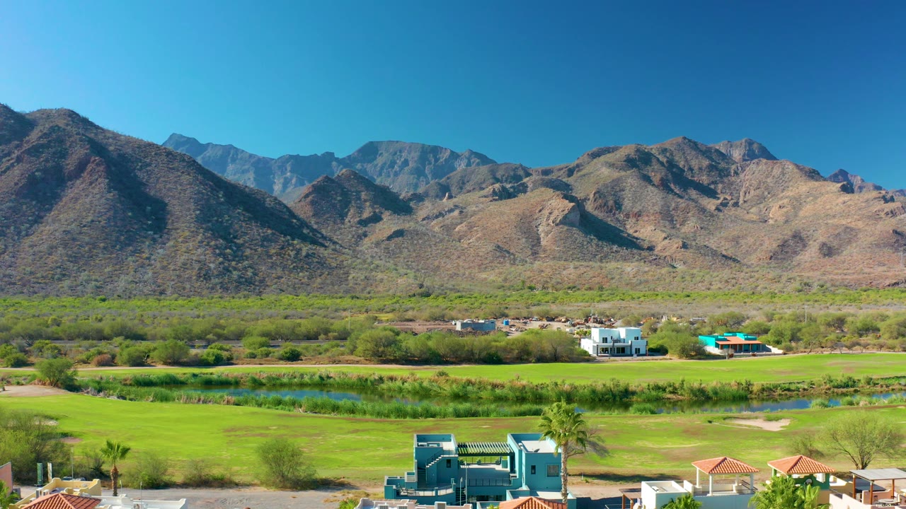 Mountain valley with green fields, water, and a blue building near the bottom.