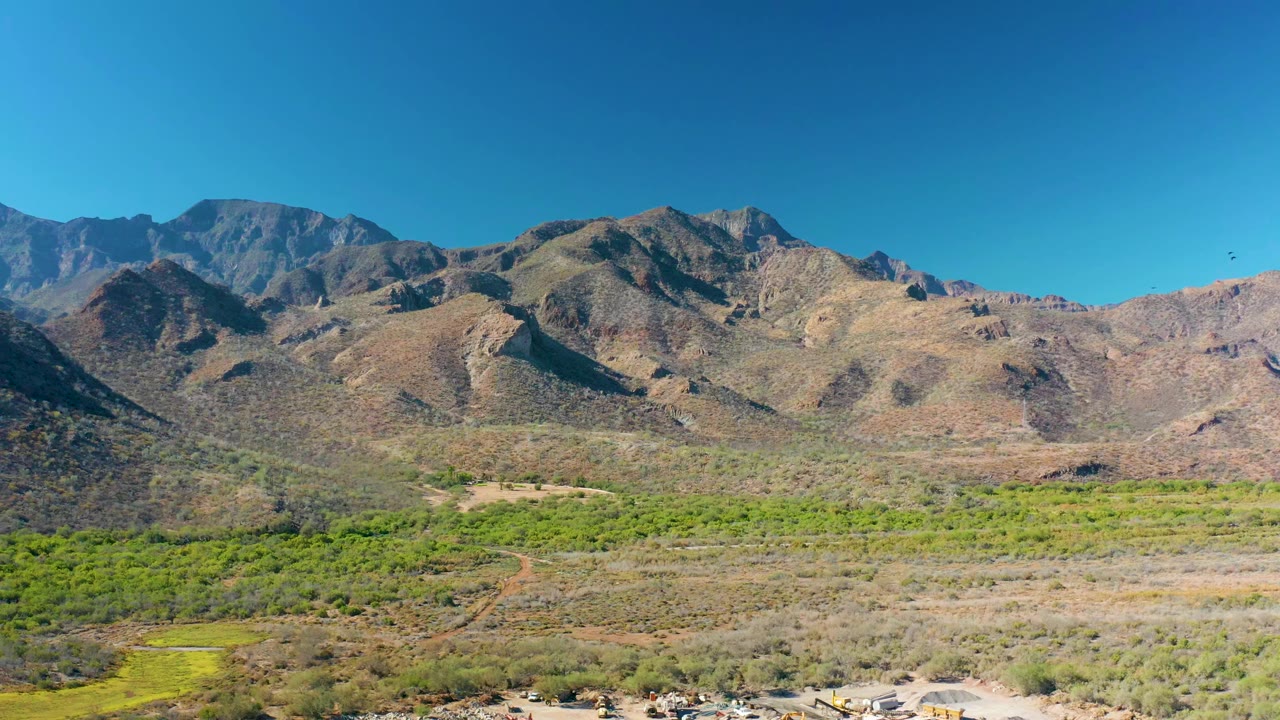 Opening frame of a wide mountain valley in Loreto, Baja California Sur, Mexico, with green scrub, brown terrain, rugged ridges, and no visible people.
