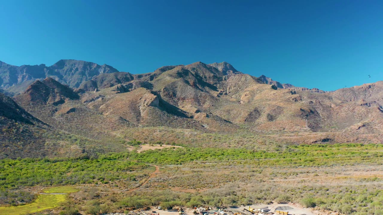 One second into the clip, the Loreto valley remains in a wide elevated view with rocky mountain slopes, green vegetation bands, dry ground, and no visible people.