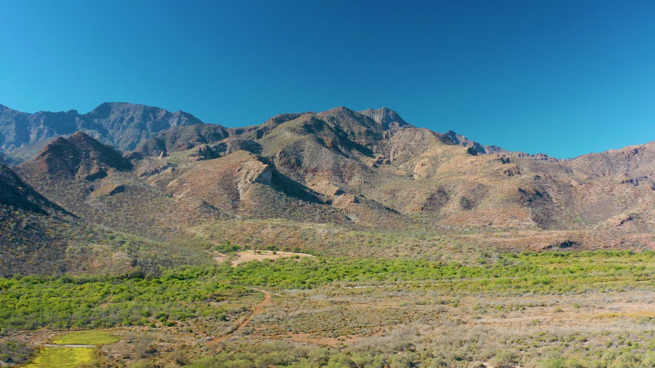 Wide aerial view of a dirt road crossing a desert valley below mountains.