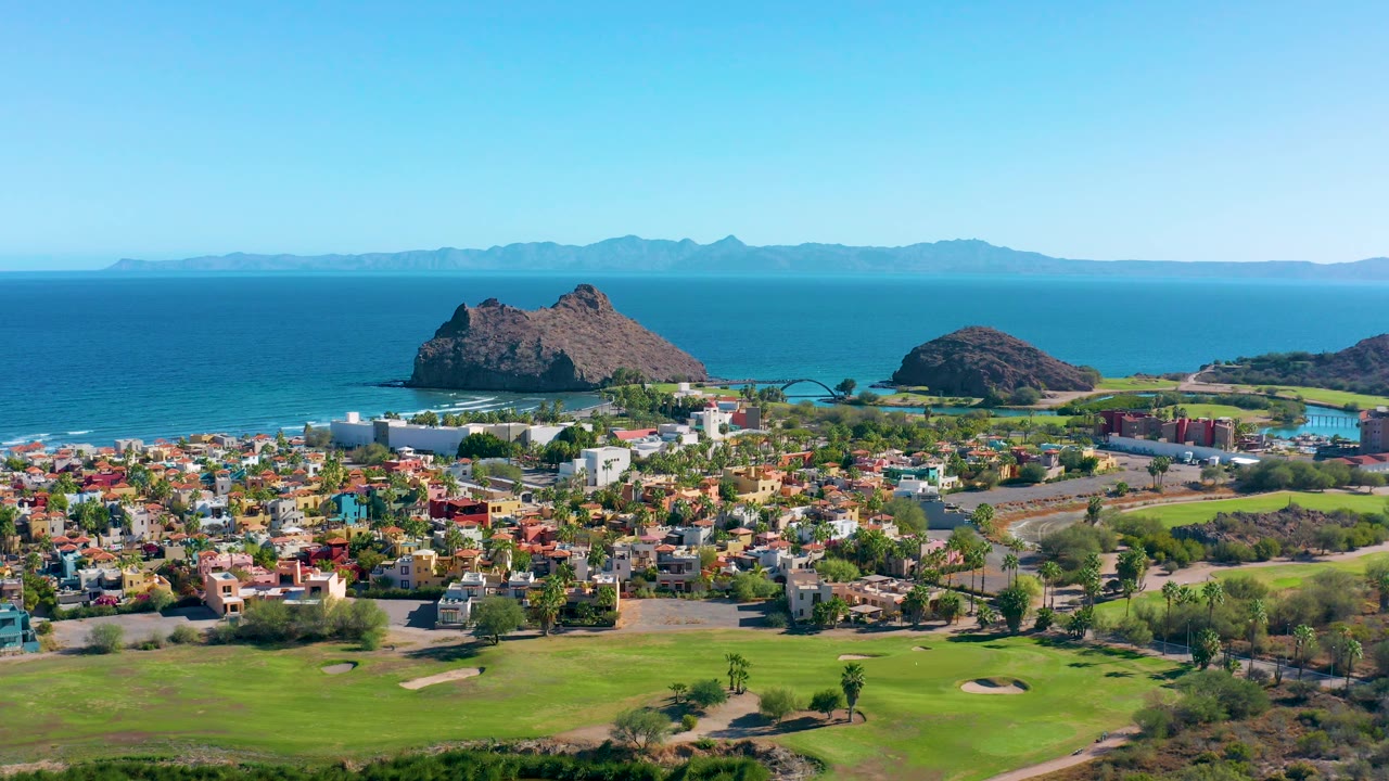 Aerial coastline view with fairways, houses, rocky islands, and open ocean.