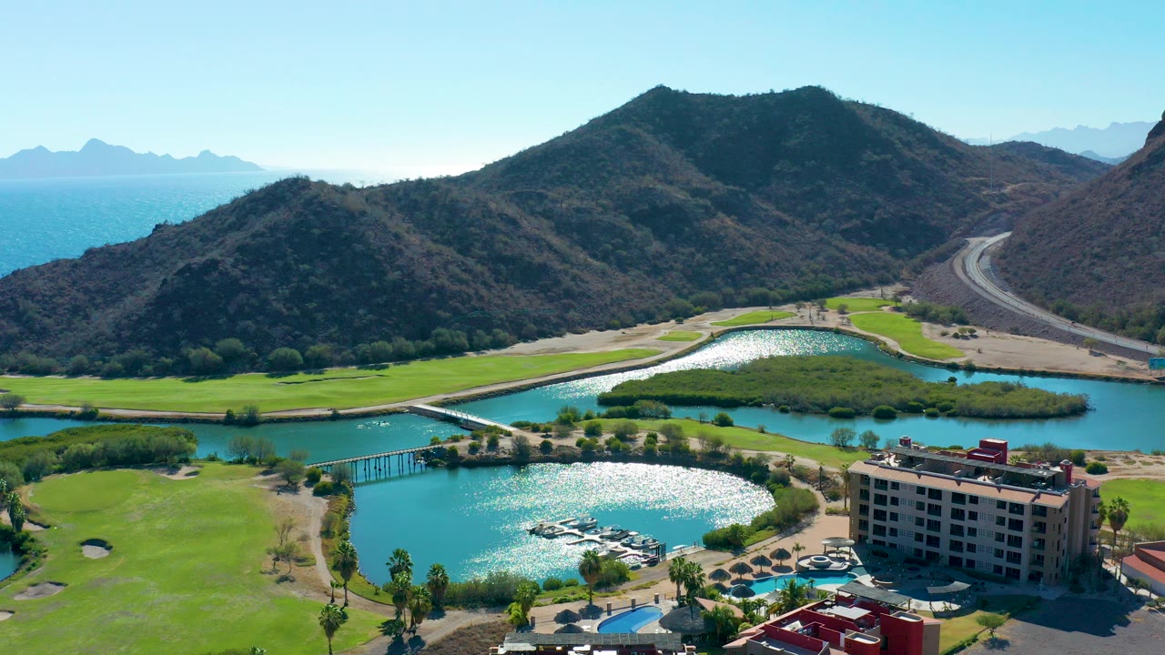 Aerial view of a lagoon, golf course, hotel, mountains, road, and ocean.