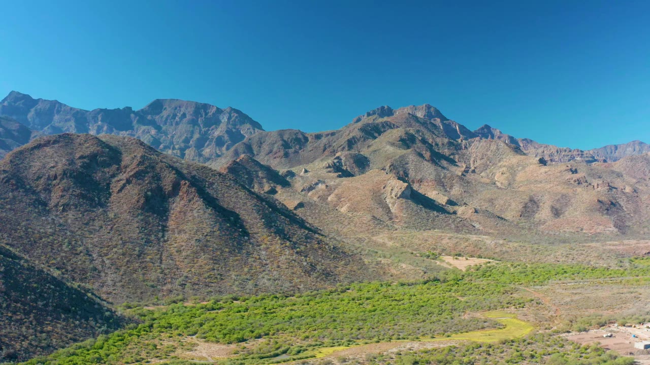 One second in, the elevated view holds on layered mountain ridges and bright green valley vegetation near Loreto, with no visible people.