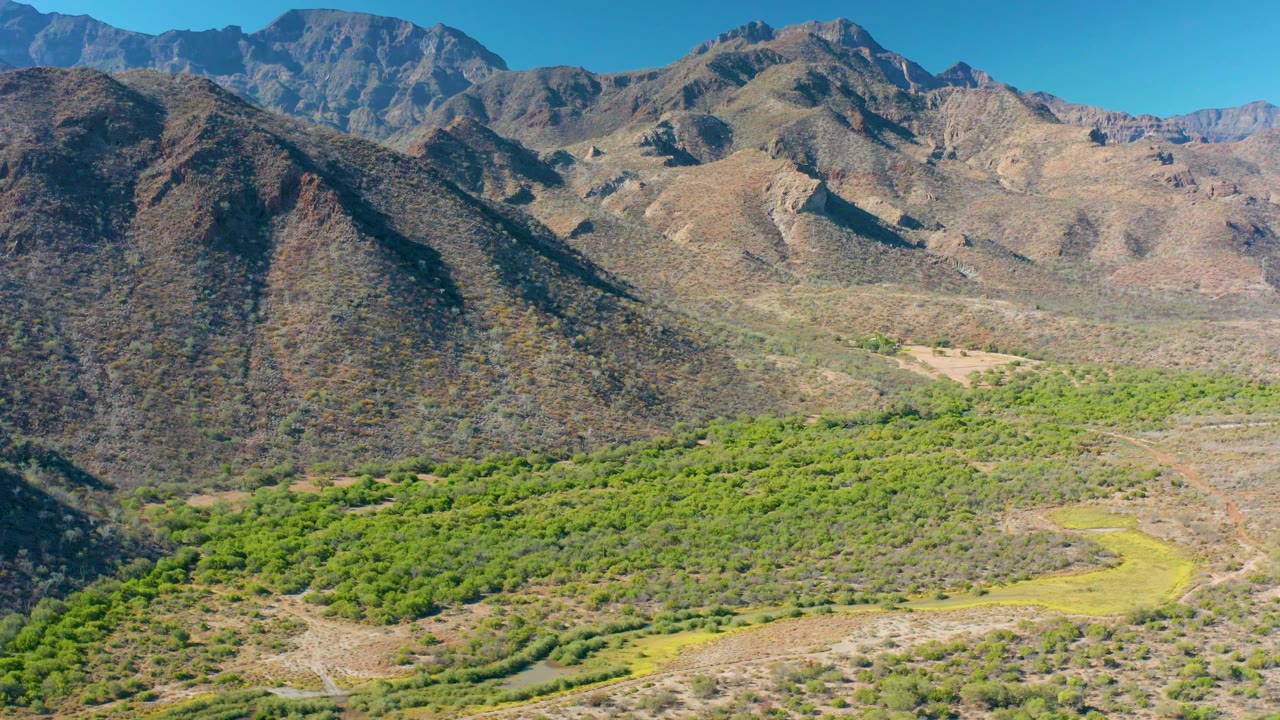 A darker rocky slope occupies the left side of the Loreto frame while green vegetation spreads across the lower valley and dry mountains rise in the distance, with no visible people.