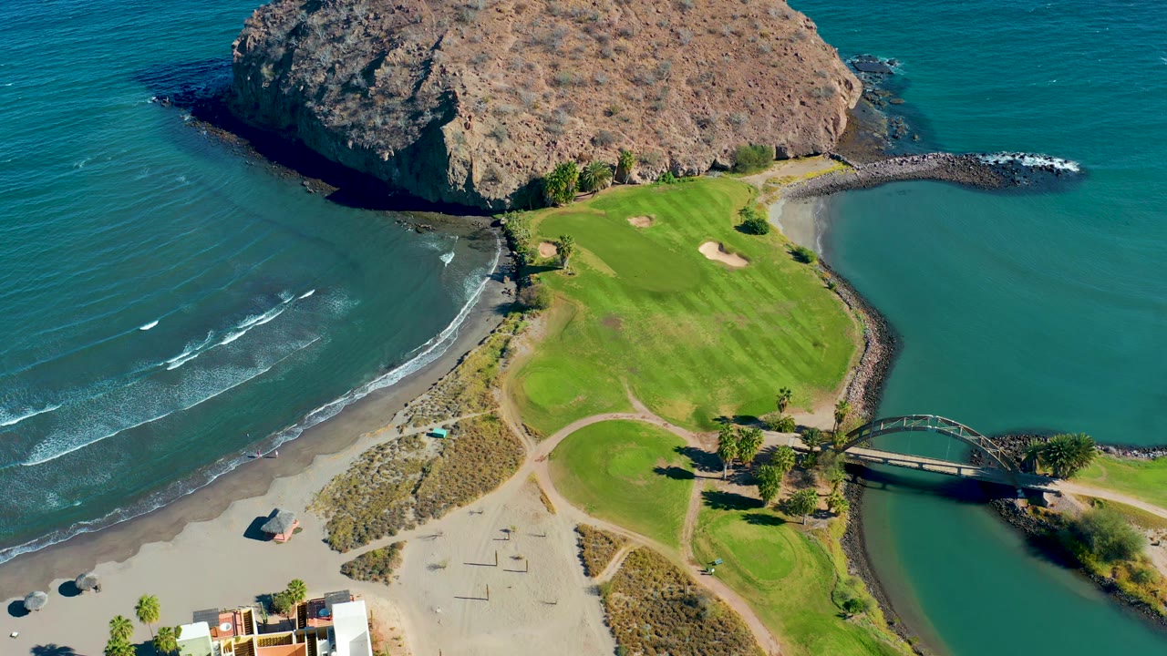 Beach and golf course seen from above beside a rocky coastal hill.
