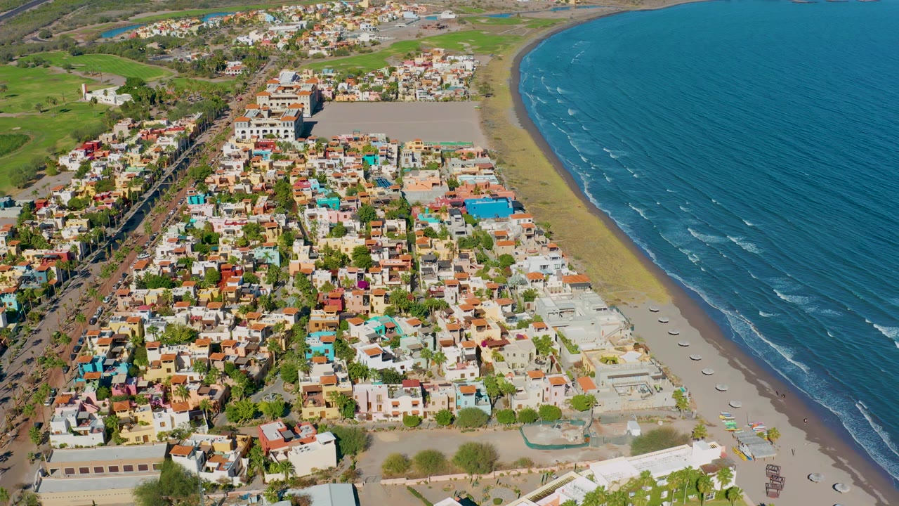 Drone view of colorful buildings, road, beach, and ocean shoreline.