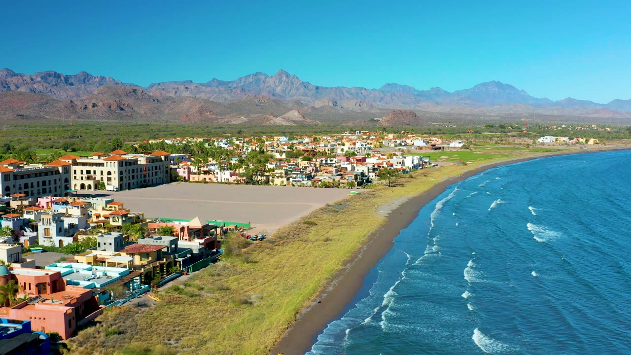 Beachfront buildings and empty sandy area beside blue ocean and mountains