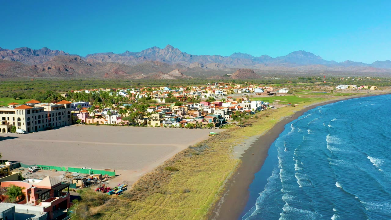Aerial beach edge with parking area, town, ocean, and mountains