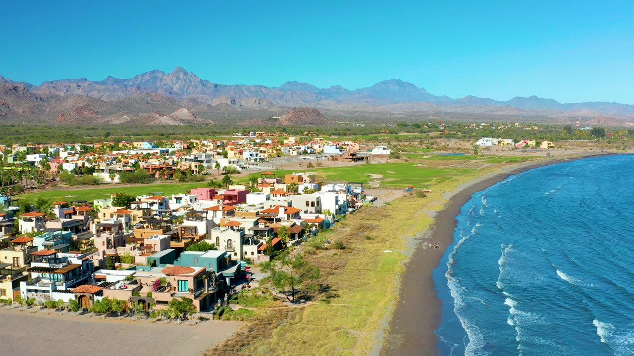 Closer aerial view of colorful homes beside beach, grass, ocean, and mountains