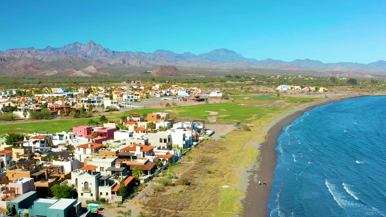 Coastal neighborhood beside a curving dark beach and blue water.
