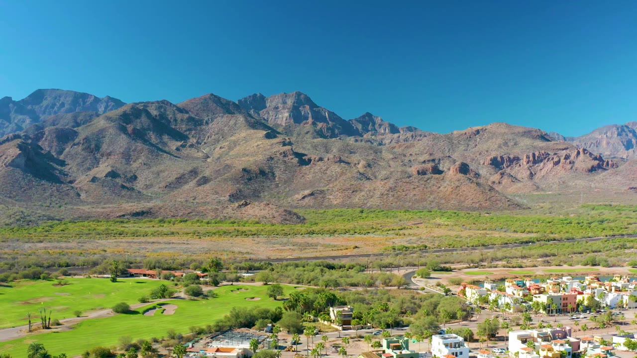 Aerial view of bright green fields below a dry mountain ridge.