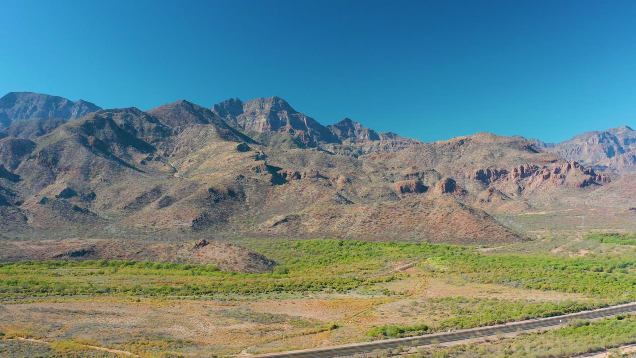 Wide desert valley with mountains, green scrub, road, and blue sky