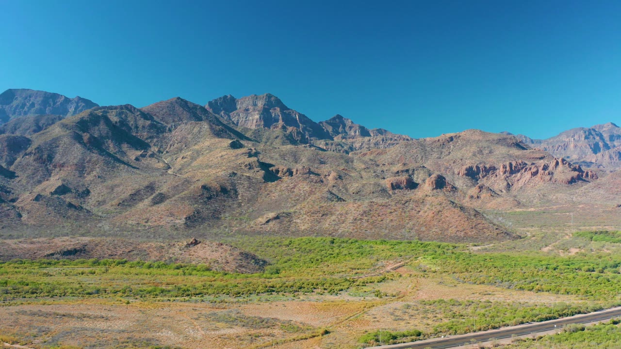 Mid-clip frame from Loreto, Baja California Sur with open desert terrain in the foreground, green vegetation across the valley, layered rocky mountains in the background, and no visible people.