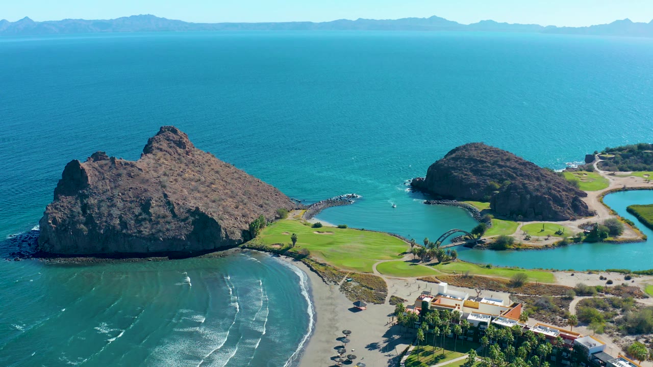 Rocky coastal islands beside a beach with wave lines and green shoreline grass.