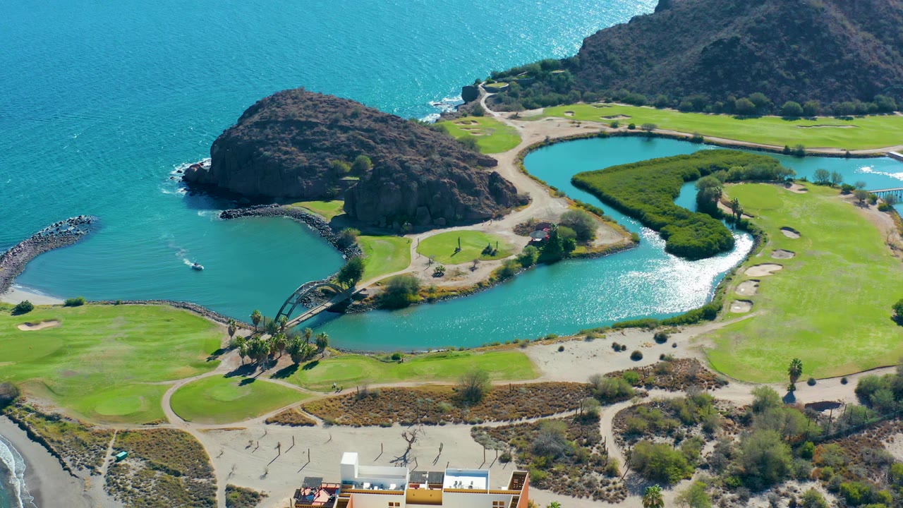 Aerial view of lagoon inlet, rocky outcrop, ocean water, green lawns, paths, and lower-edge building