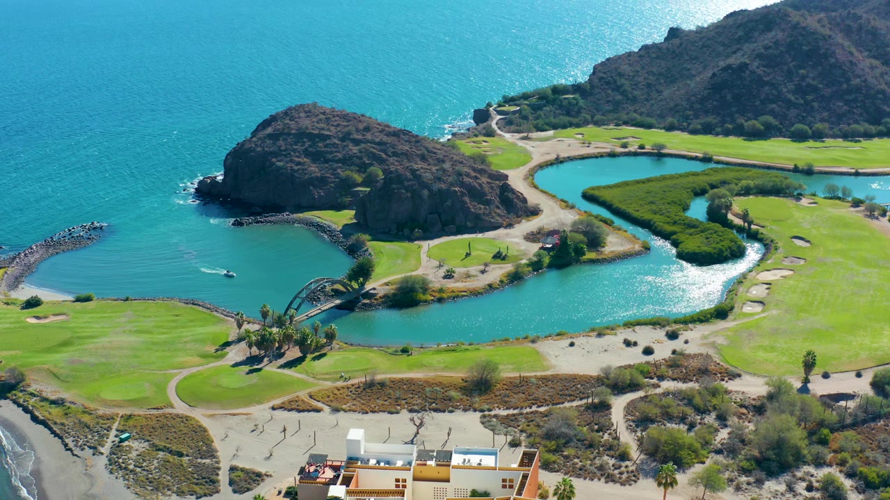 Aerial coastal course view with a central lake, rocky point, and ocean water.