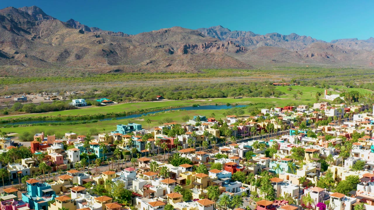 Aerial neighborhood edge with fields, river, and rocky mountains.