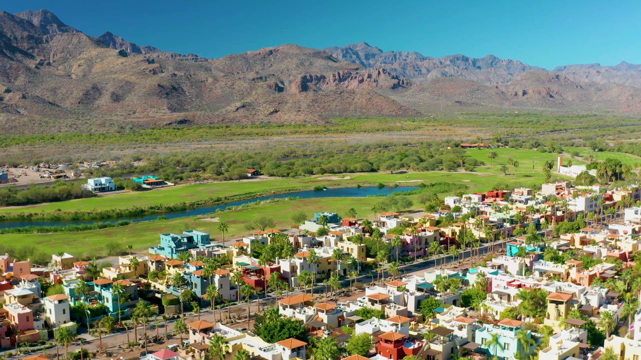 Wide aerial view of residential blocks beside green fields and mountains.