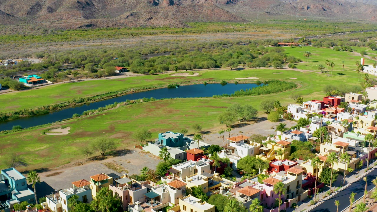 Loreto aerial frame with the pond centered across the golf course, fairways and sand traps around it, residential buildings gathered at the lower right, and no visible people.