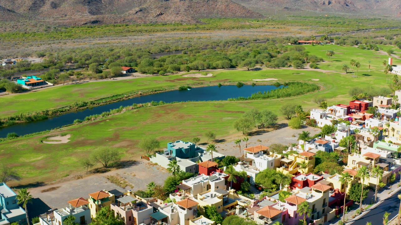 Wide aerial of a golf course pond, fairways, homes, and mountains.