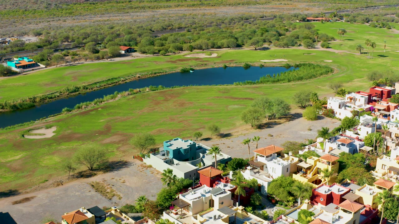 Drone-height frame over Loreto, Baja California Sur showing a green golf fairway, the long pond near the top, and clustered homes along the lower right.