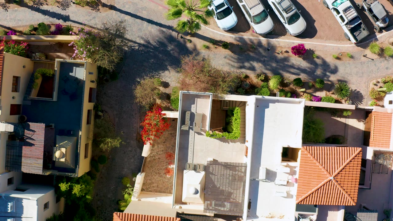 Loreto overhead frame showing the residential street, cars near the curb, white and tan rooftops, dry planting beds, bougainvillea color, and no visible people.