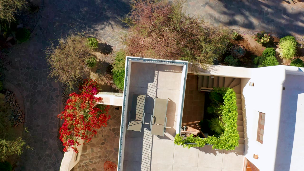 Aerial view of patio chairs, white walls, red flowers, and shaded stone path.