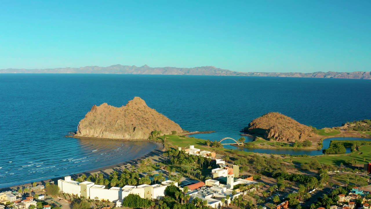 Wide aerial view of rocky shore, sandy beach, town edge, and calm sea.