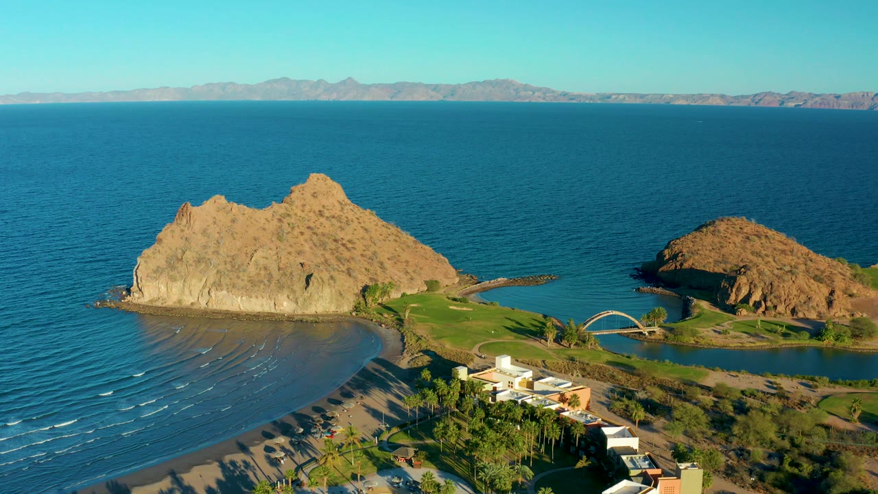 Wide aerial of ocean, rocky outcrops, beach, and resort buildings.