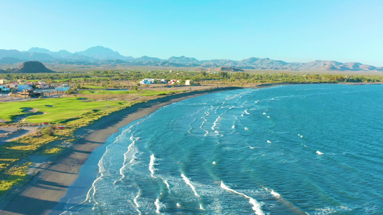 Aerial shoreline scene with dark sand in the foreground and bright green land beside the bay.