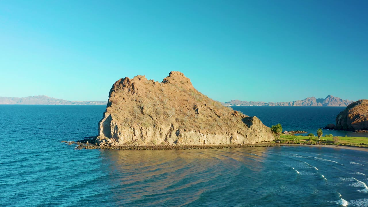 Loreto, Baja California Sur aerial view with the rocky outcrop slightly right of center, turquoise water across the foreground, distant landforms under a clear sky, and no visible people.