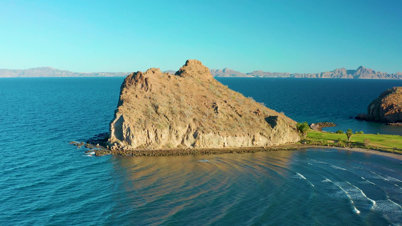 Rock outcrop, ocean, beach edge, and mountain horizon.