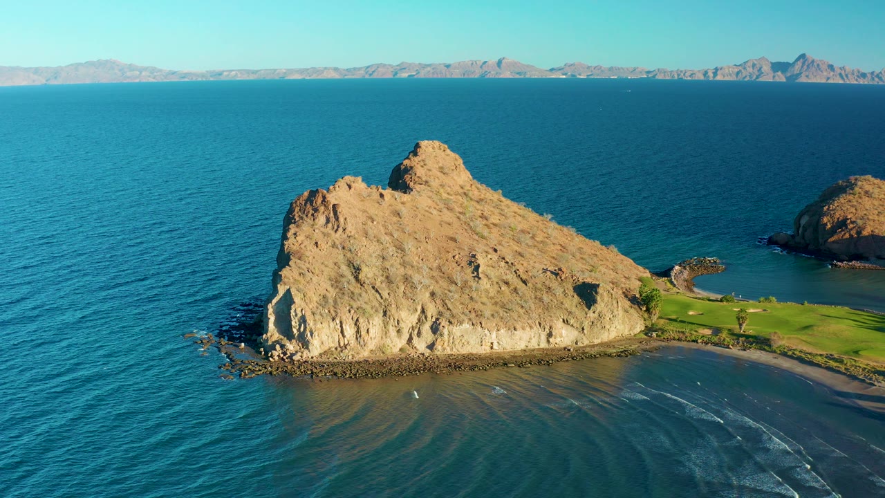 Rocky shoreline with blue ocean and sandy shallows.