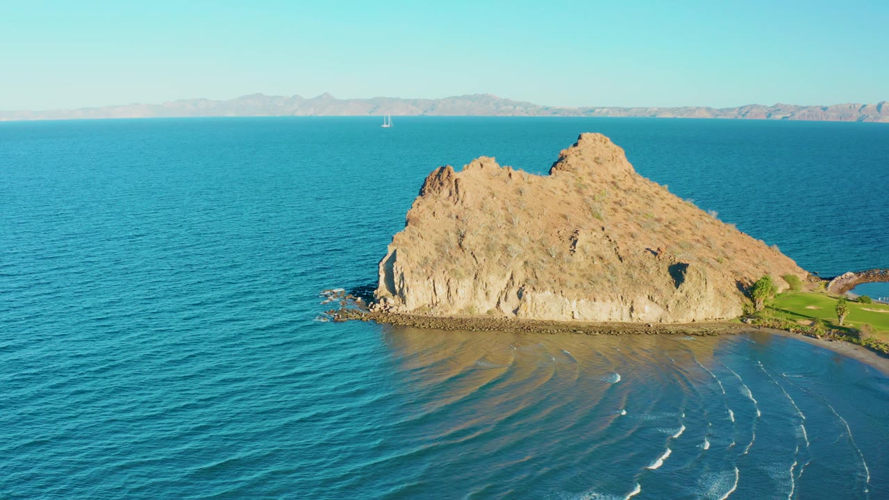 Tan rock island in turquoise water under a clear sky.