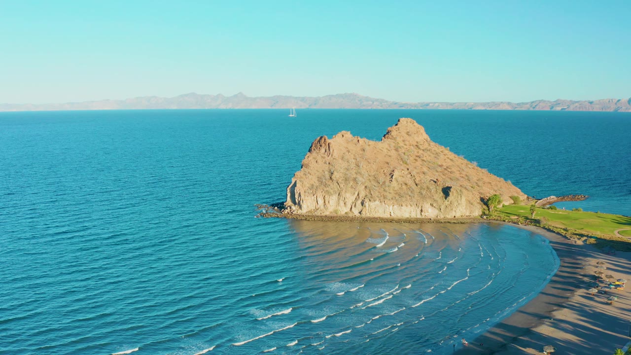 Rocky coastal outcrop with small waves curving toward a sandy beach.